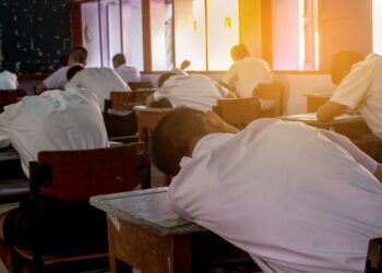 Poor Student with student’s uniform so tired of the exam. Lying down on the arm in the classroom. Sleepy student fall asleep during test at noon in the hot season.