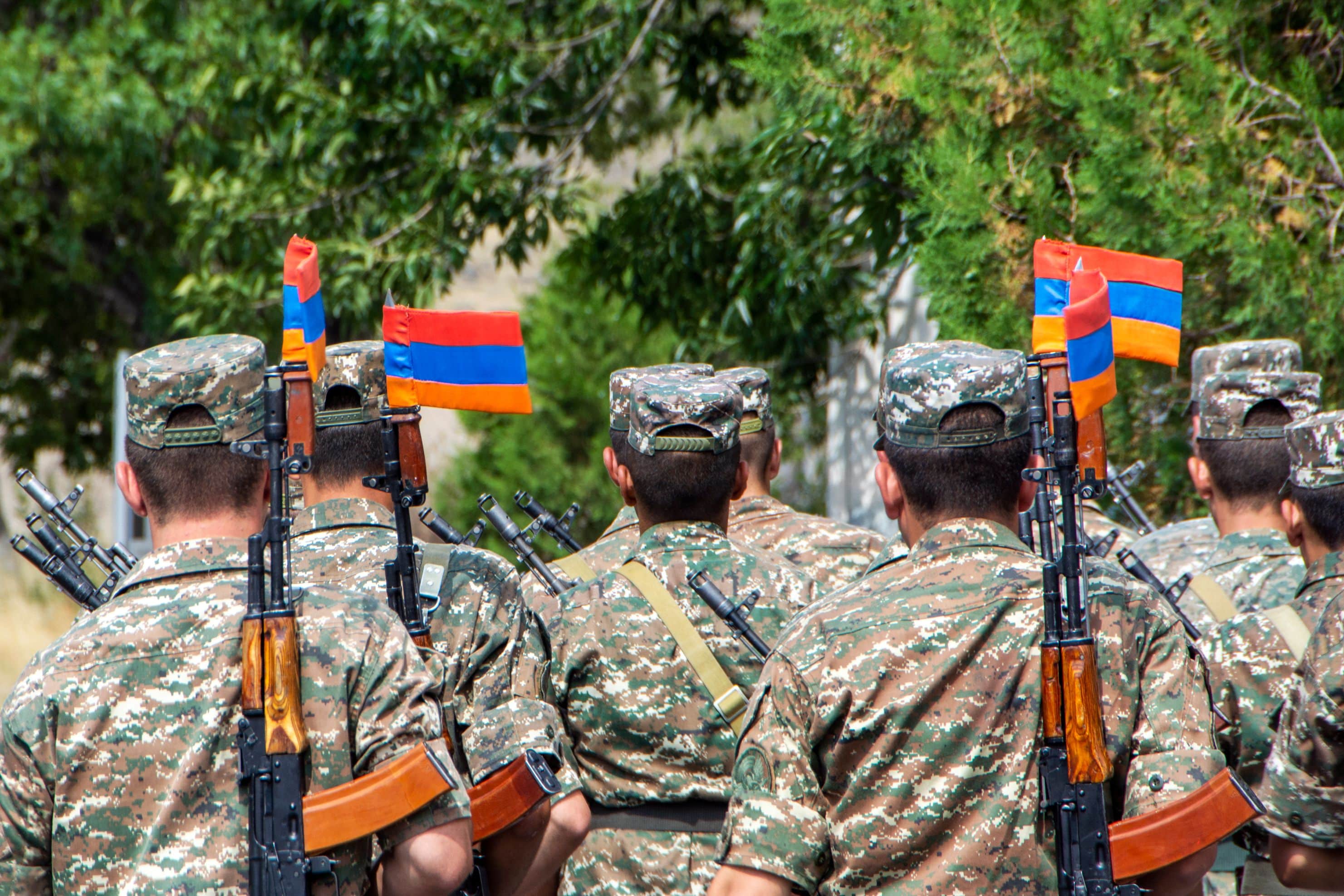 A squad of Armenian soldiers marching with automatic guns and Armenian flags attached to the bayonet knives. Back view with green trees on blurred background, Armenia