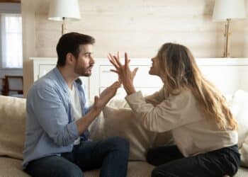 Emotional annoyed stressed couple sitting on couch, arguing at home. Angry irritated nervous woman man shouting at each other, figuring out relations, feeling outraged, relationship problems concept.