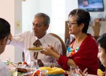 A married couple lives together during a family dinner in Mexico. An adult woman holds a plate while her husband serves her tacos during a family reunion to celebrate Mexican independence.