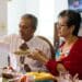A married couple lives together during a family dinner in Mexico. An adult woman holds a plate while her husband serves her tacos during a family reunion to celebrate Mexican independence.