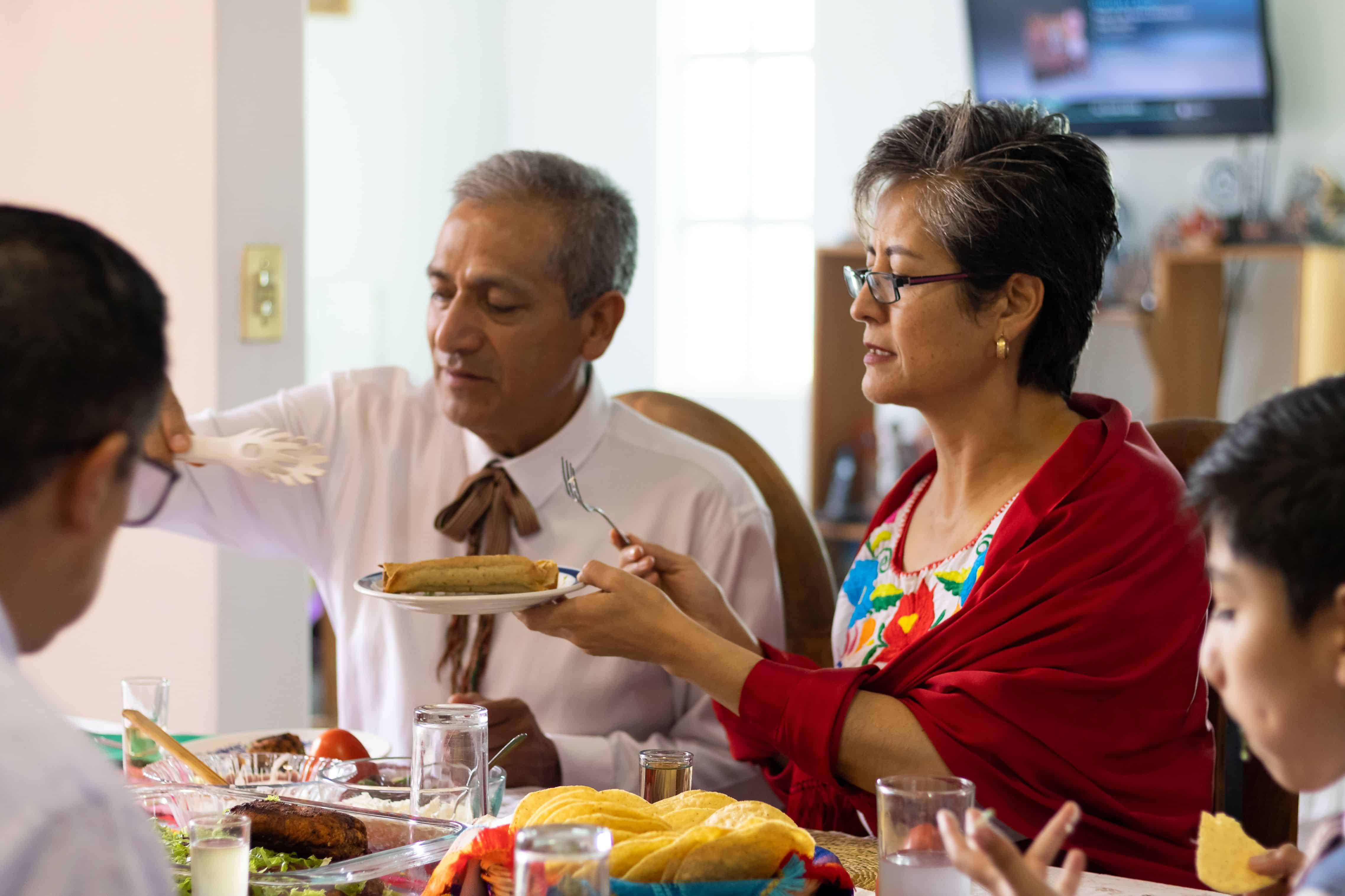 A married couple lives together during a family dinner in Mexico. An adult woman holds a plate while her husband serves her tacos during a family reunion to celebrate Mexican independence.