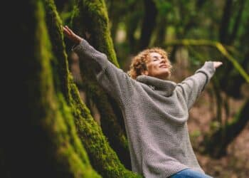 Overjoyed happy woman enjoying the green beautiful nature woods forest around her - concept of female people and healthy natural lifestyle - happiness emotion and adult lady opening arms