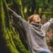 Overjoyed happy woman enjoying the green beautiful nature woods forest around her - concept of female people and healthy natural lifestyle - happiness emotion and adult lady opening arms