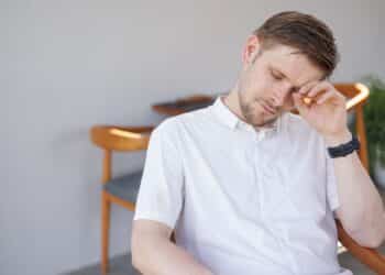 A tired man in a white shirt is sitting in a cafe. Summer heat exhaustion. Burnout syndrome from hard work. Vacation and business trip. Poor sleep routine and quality of cortisol