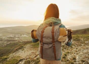 Hiker woman with backpack and sleeping bag walking in the mountains in summer at sunset