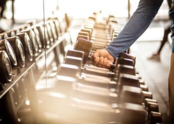 Muscular build sportsman taking weights from a rack in a gym. Focus is on hand. Close up.