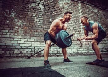 Two muscular athletes training, one raise the bar when other is motivating. Scream. Working hard. Street gym. Exercise for the muscles of the back