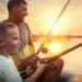 Happy Father and Son together fishing from a boat at sunset time in summer day under beautiful sky on the lake.