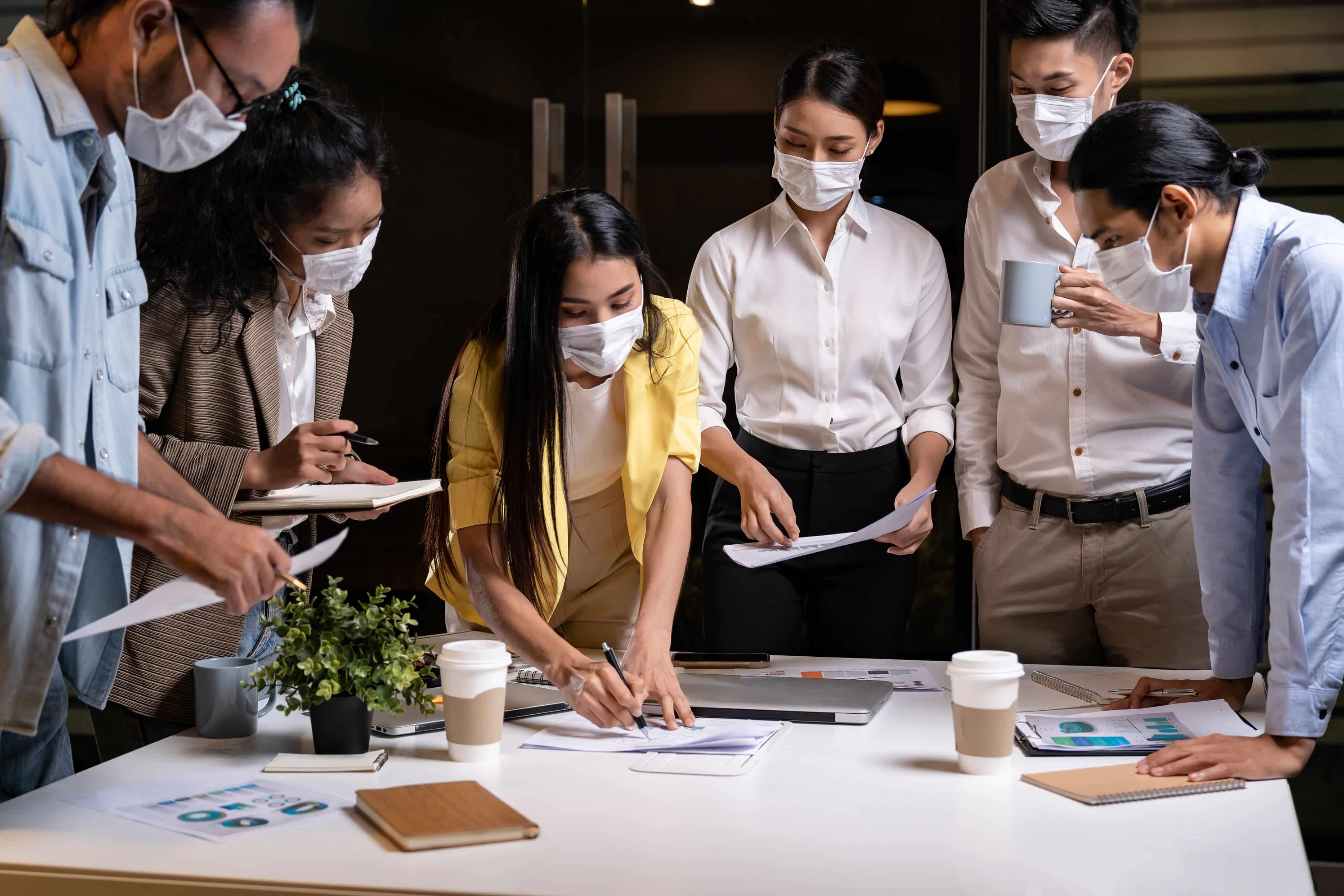 Work late concept of Interracial asian business team brainstorm idea at office meeting room at night. They wear face mask reduce risk to infection of COVID-19 coronavirus as new normal lifestyle.