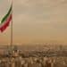 Iran flag waving in the wind above skyline of Tehran lit by orange glow of sunset.