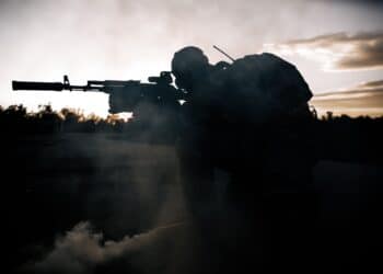 Military man in a gas mask sitting on concrete aiming at a sniper rifle