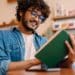 Young indian handsome man in glasses reading book at cafe