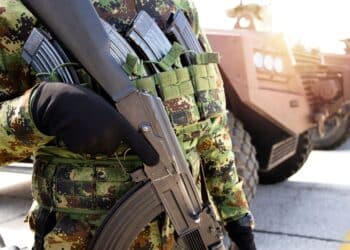 Portrait of an unrecognizable soldier in camouflage uniform armed with rifle and standing by transporter vehicle.