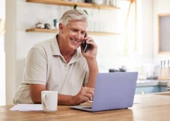 Senior man, phone call and laptop home budget finances, online banking and planning for retirement savings, investment and insurance. Happy mature guy working, consulting and mobile admin connection