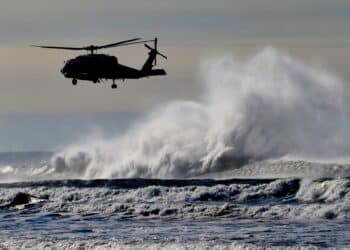 LONG BEACH, US - Apr 19, 2021: A vertical of the silhouette of a helicopter flying above the big foamy waves at the Washington Coast