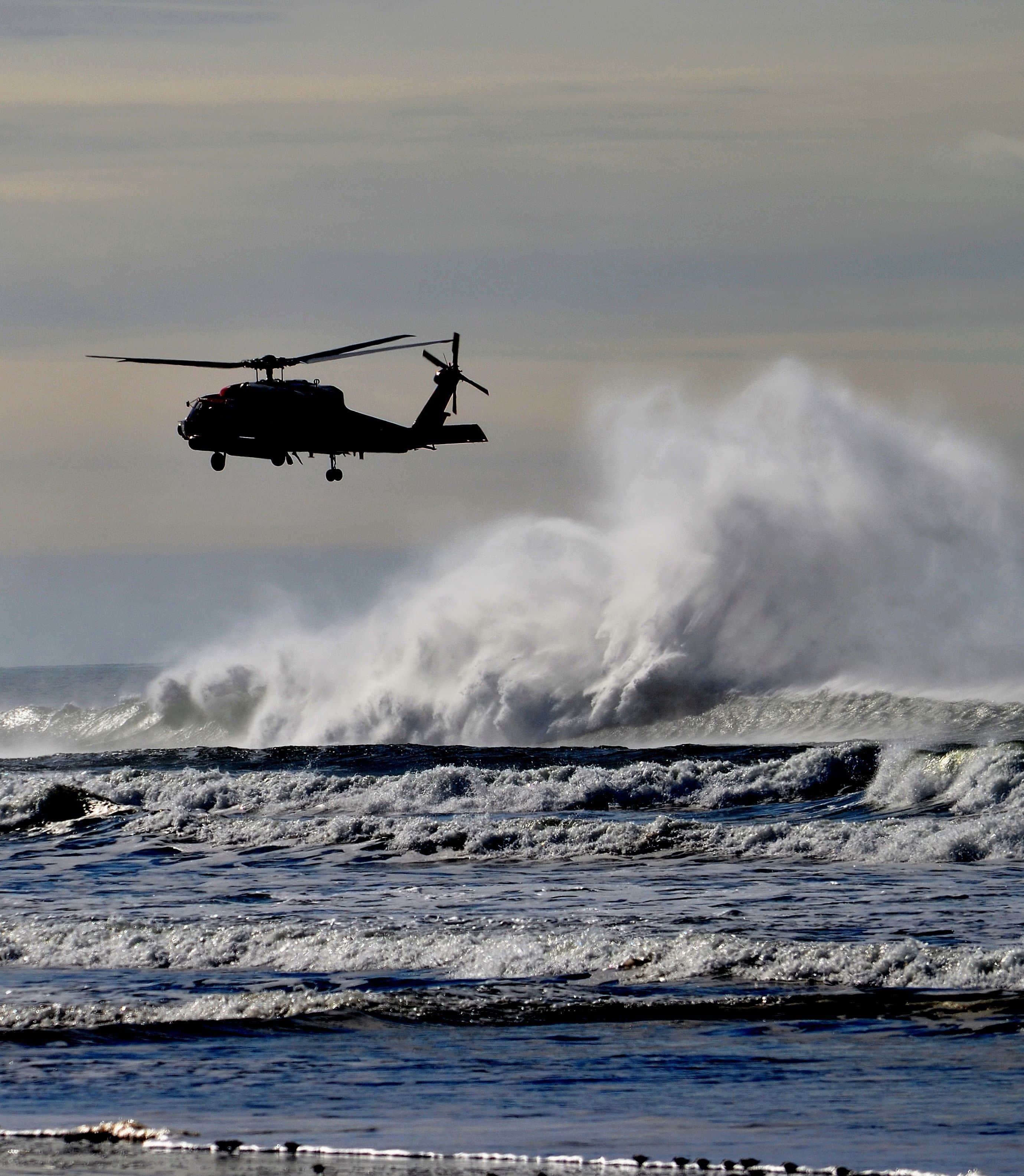 LONG BEACH, US - Apr 19, 2021: A vertical of the silhouette of a helicopter flying above the big foamy waves at the Washington Coast