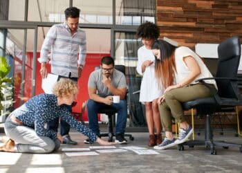 Creative people looking at project plan laid out on floor. Mixed race business associates discussing new project plan in modern office.