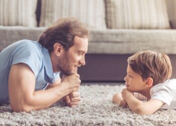 Side view of handsome father and his cute son looking at each other and smiling while spending time together at home
