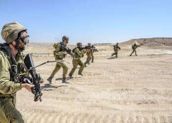 MILITARY TRAINING ZONE, ISRAEL - JUNE 17, 2015: Israeli army combat commando squad firing while charging on terror targets. Infantry soldiers running & shooting during desert military combat training.