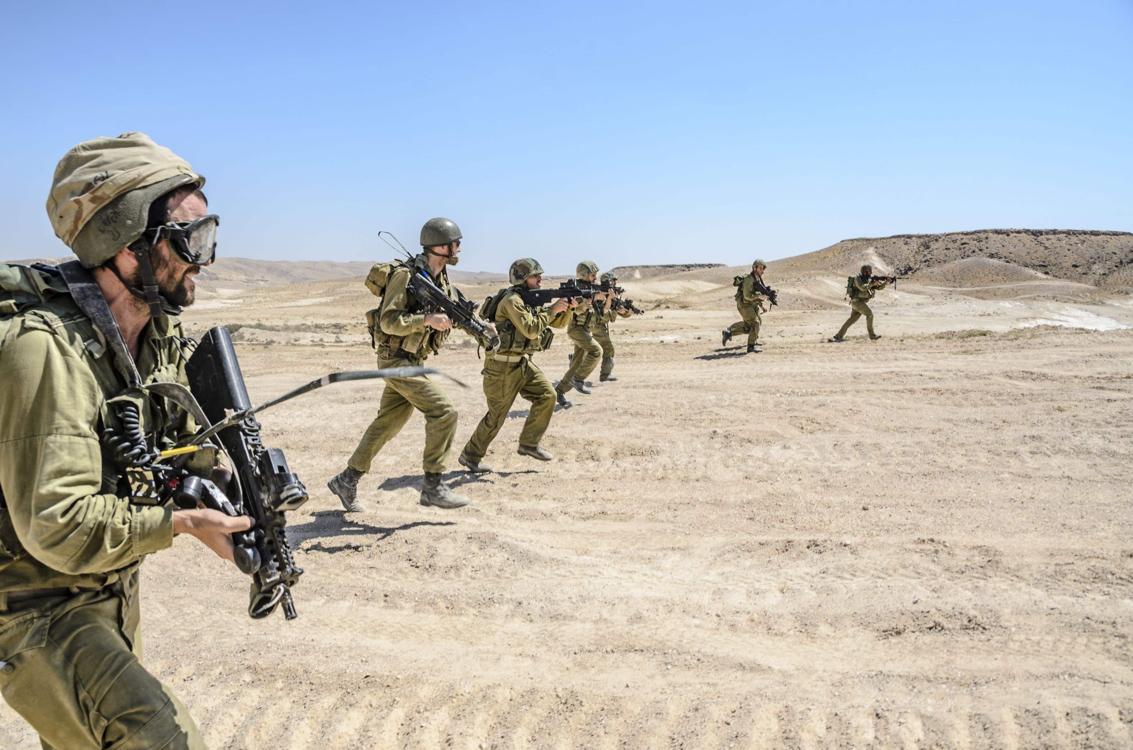 MILITARY TRAINING ZONE, ISRAEL - JUNE 17, 2015: Israeli army combat commando squad firing while charging on terror targets. Infantry soldiers running & shooting during desert military combat training.