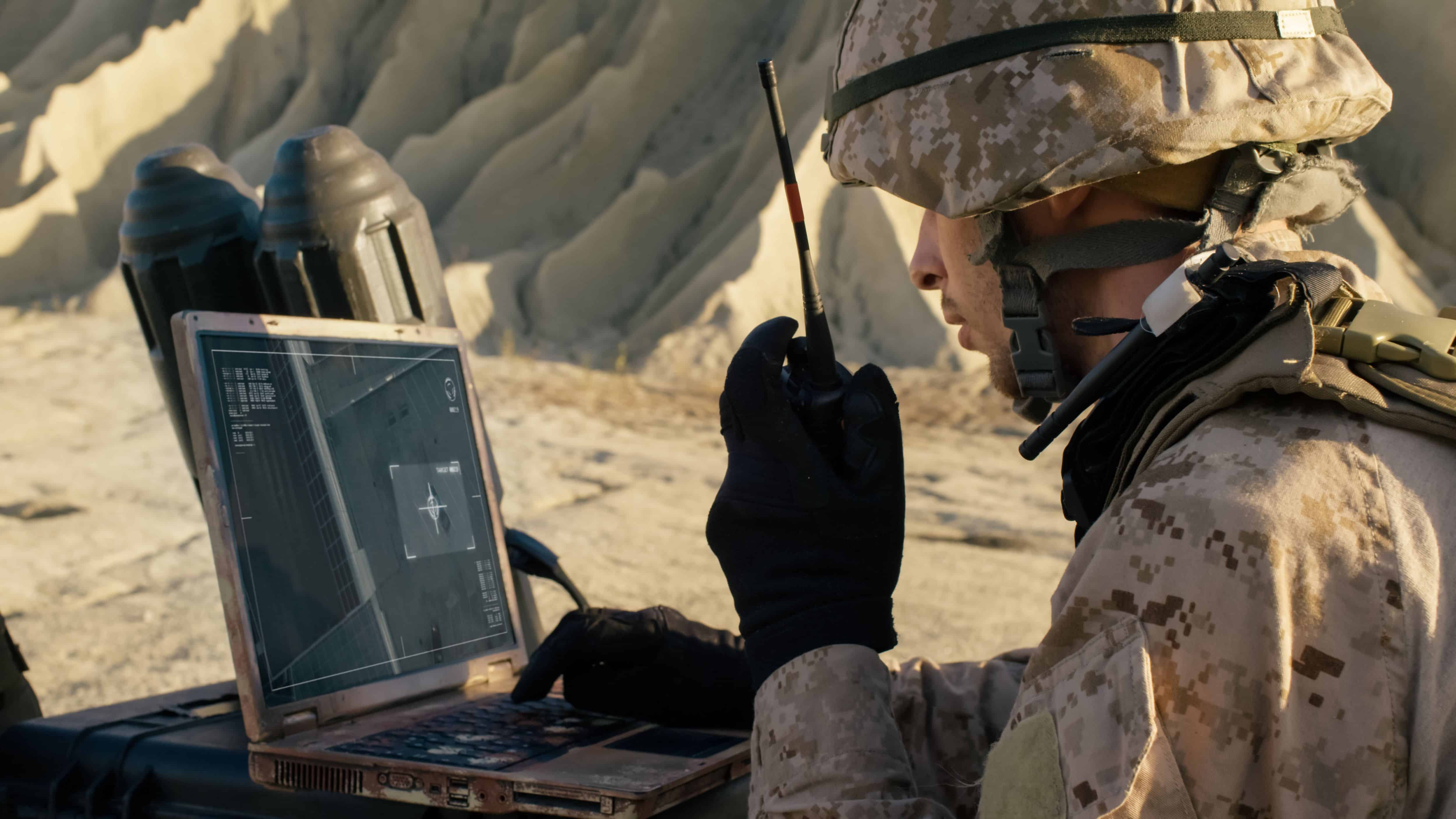 Soldier is Using Laptop Computer for Tracking the Target and Radio for Communication During Military Operation in the Desert