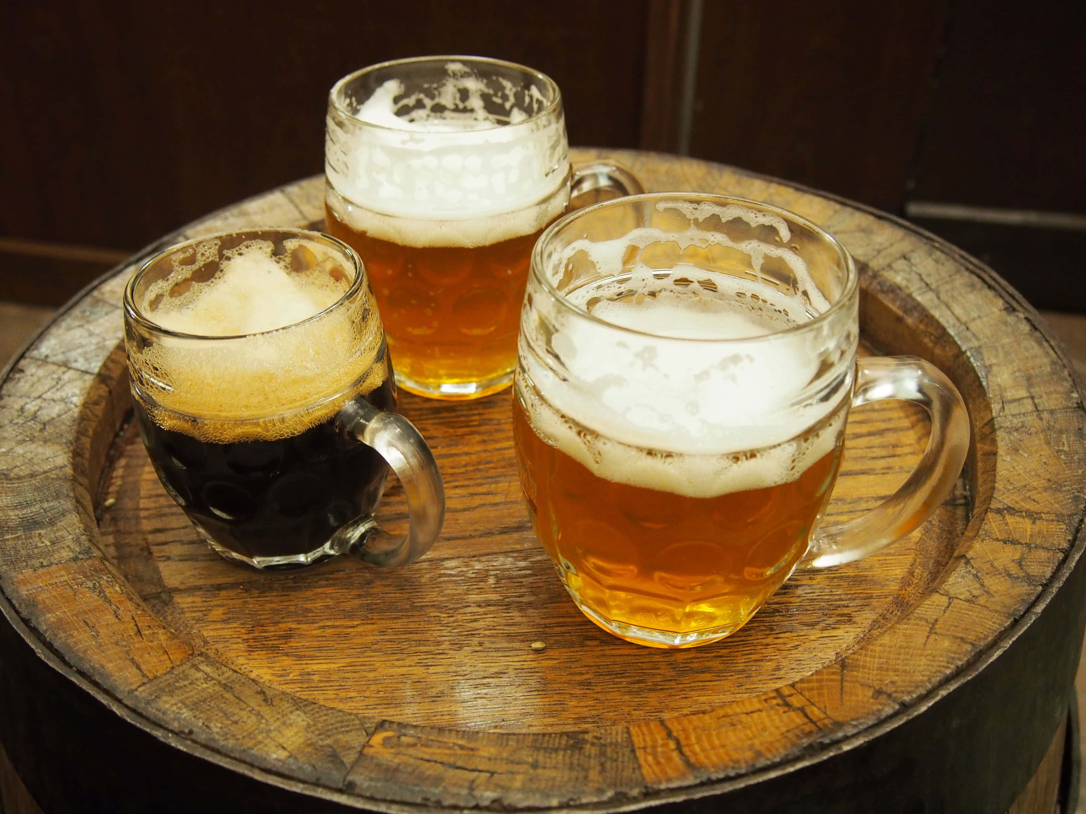 Three Glasses of Czech Beer Resting on a Wooden Barrel Table, Unfiltered Pilsner Style Lager, Two Half Litres of Light and One Small Glass of Dark, all Partly Drunk