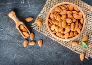 Top view of almonds on dark stone table with wood spoon or scoop. Almond in wooden bowl. Nuts freely laid on dark board.