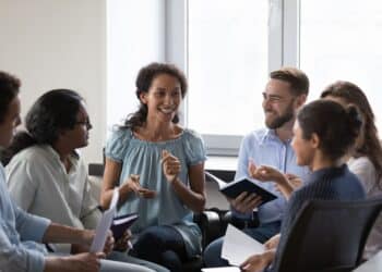 Happy diverse addicts sitting on chairs in circle, talking on group therapy meeting, discussing addiction, mental health problems. Multiethnic employees brainstorming on team training