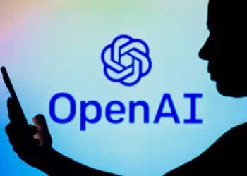 October 7, 2022, Brazil. In this photo illustration, the OpenAI logo is seen in the background of a silhouetted woman holding a mobile phone