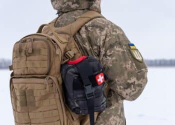 Ukrainian military man in winter uniform with tactical backpack and first aid kit on duty near combat positions. a soldier holds the straps of a duffel bag with his hands, close-up. military equipment
