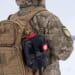 Ukrainian military man in winter uniform with tactical backpack and first aid kit on duty near combat positions. a soldier holds the straps of a duffel bag with his hands, close-up. military equipment