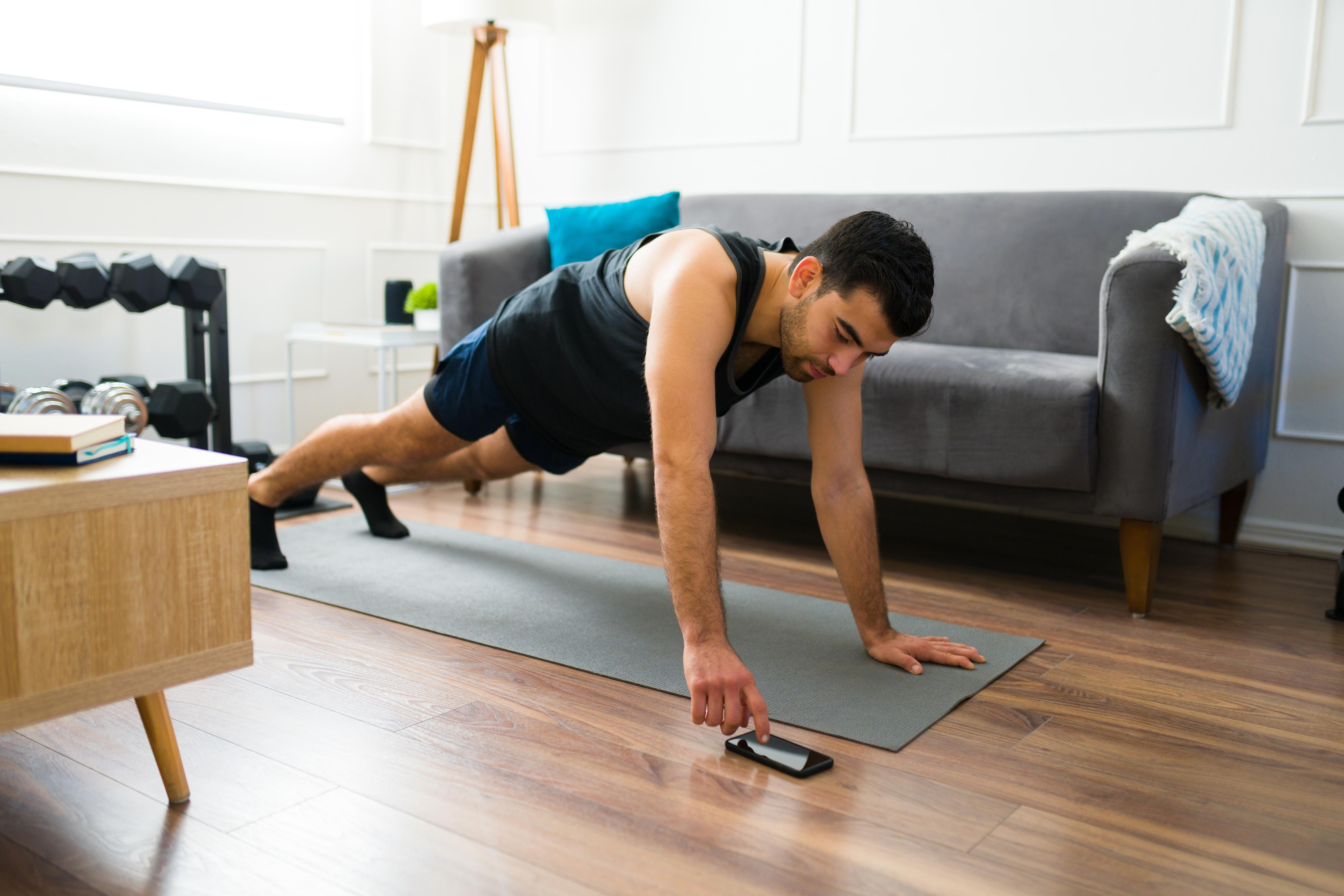Healthy young man with a fitness lifestyle doing a plank and using the timer app on his smartphone