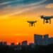 Two drone quad copters with high resolution digital camera flying aerial over spectacular sunset orange sky. Cityscape silhouette with sun goes down in the background.Vehicle at sundown and copy space