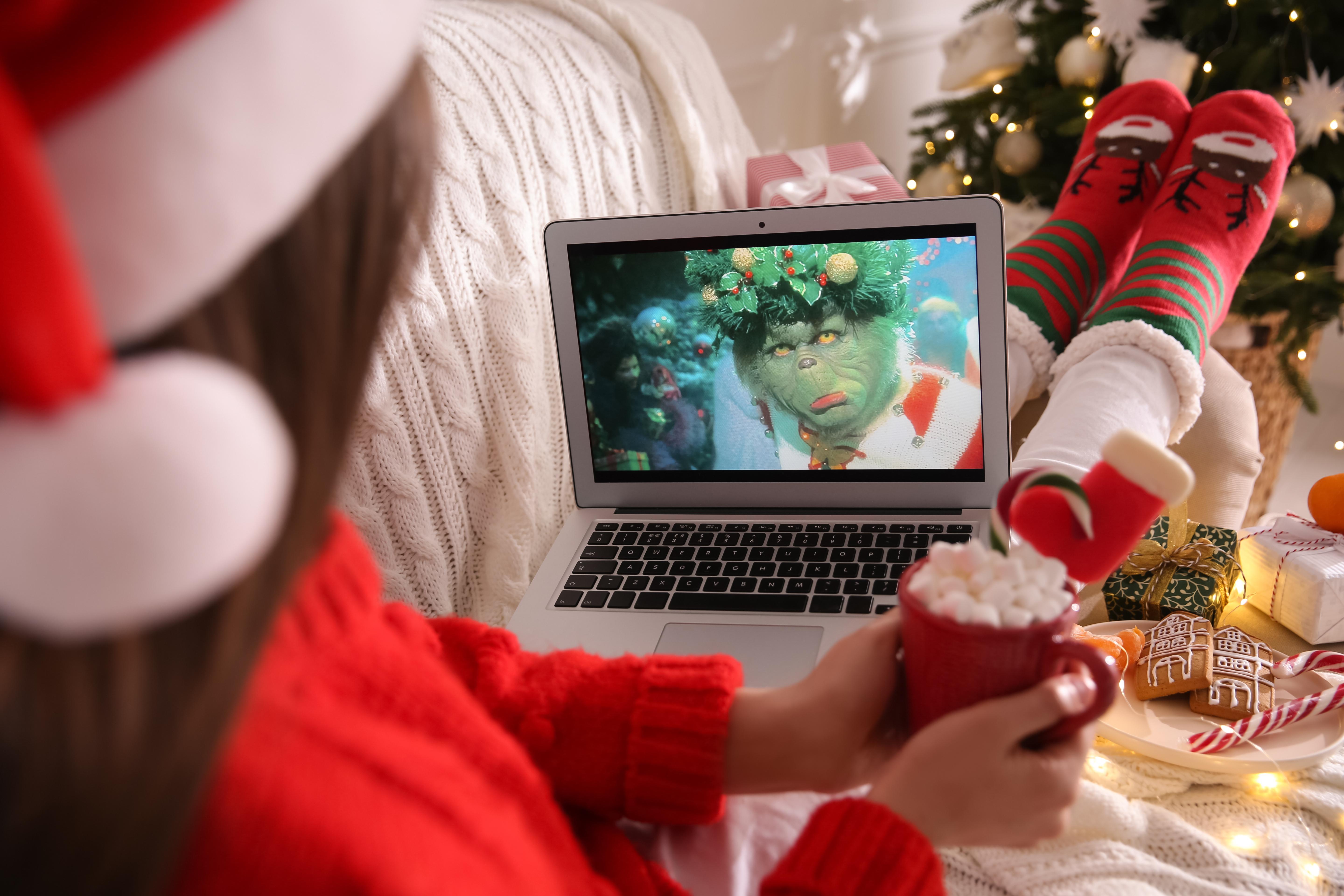 MYKOLAIV, UKRAINE - DECEMBER 25, 2020: Woman with sweet drink watching The Grinch movie on laptop at home, closeup. Cozy winter holidays atmosphere