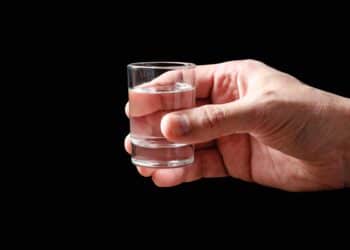 A glass of vodka in a man's hand. Black background. Copy space