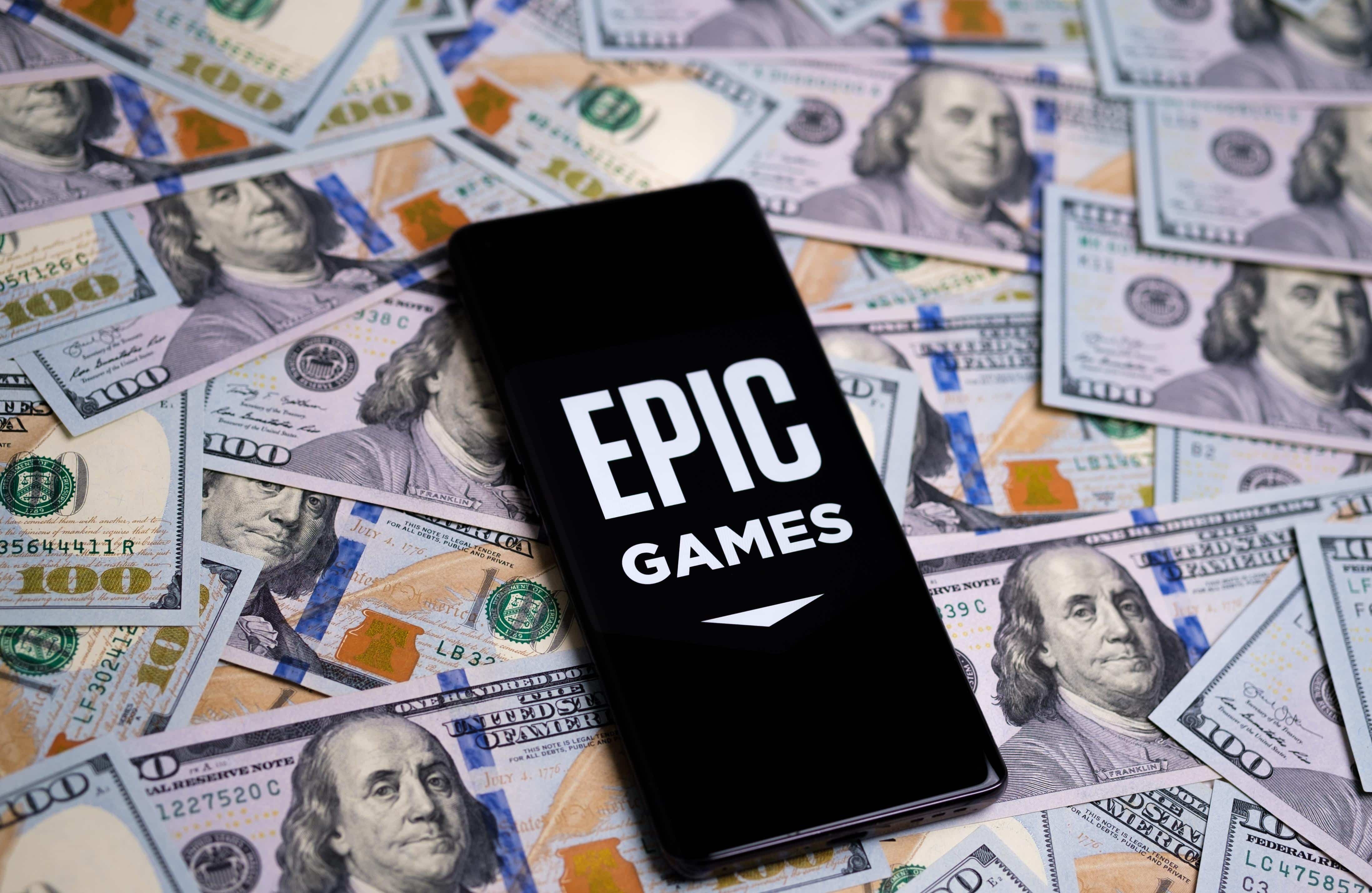 Epic Games logo seen on smartphone placed on the pile of 100 dollar banknotes. Concept for investment and profit. Shallow depth of field. Stafford, United Kingdom, April 11, 2022.