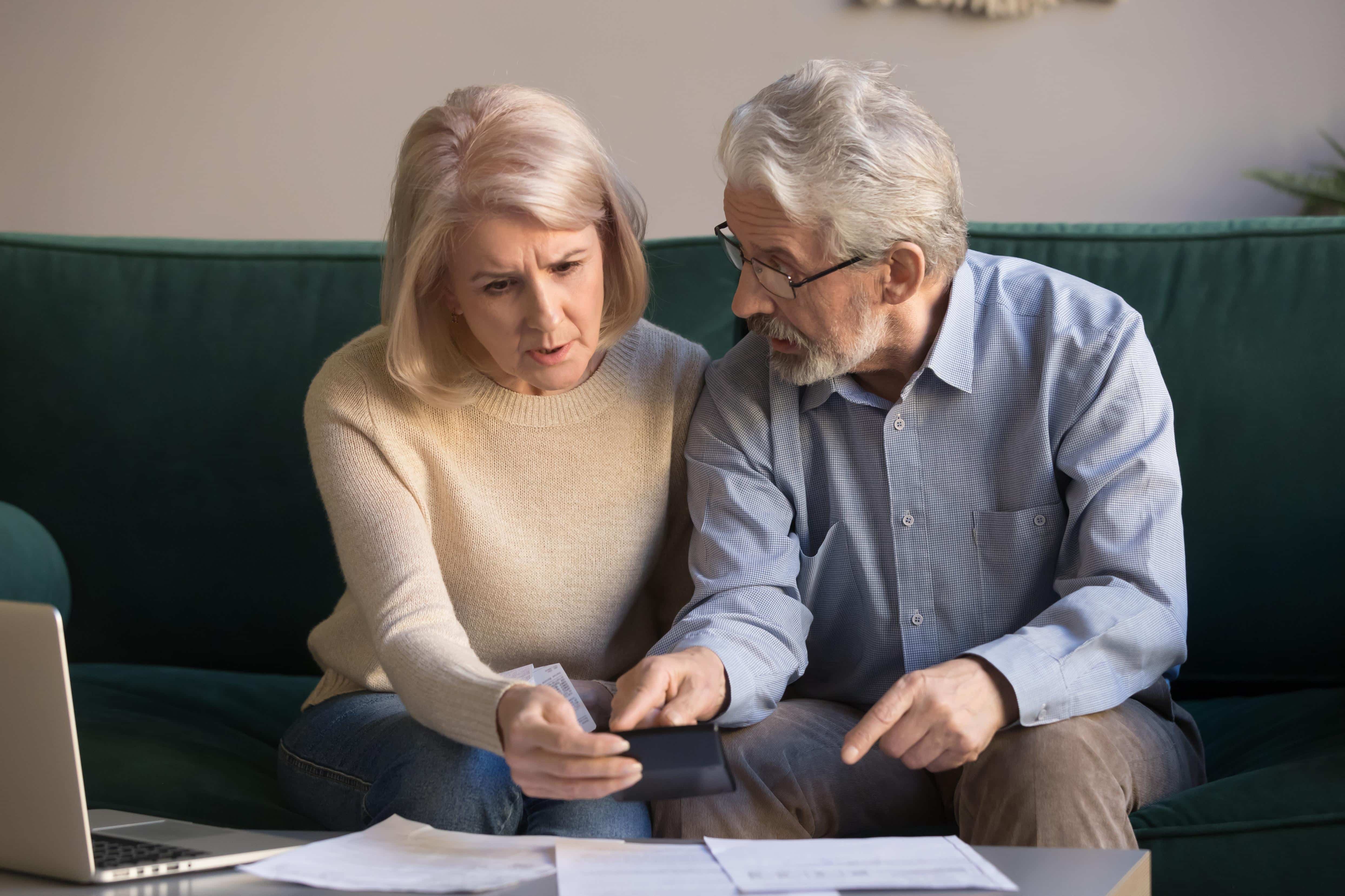Serious stressed senior old couple worried about paperwork discuss unpaid bank debt calculate bills, shocked poor retired family looking at calculator counting loan payment upset about money problem
