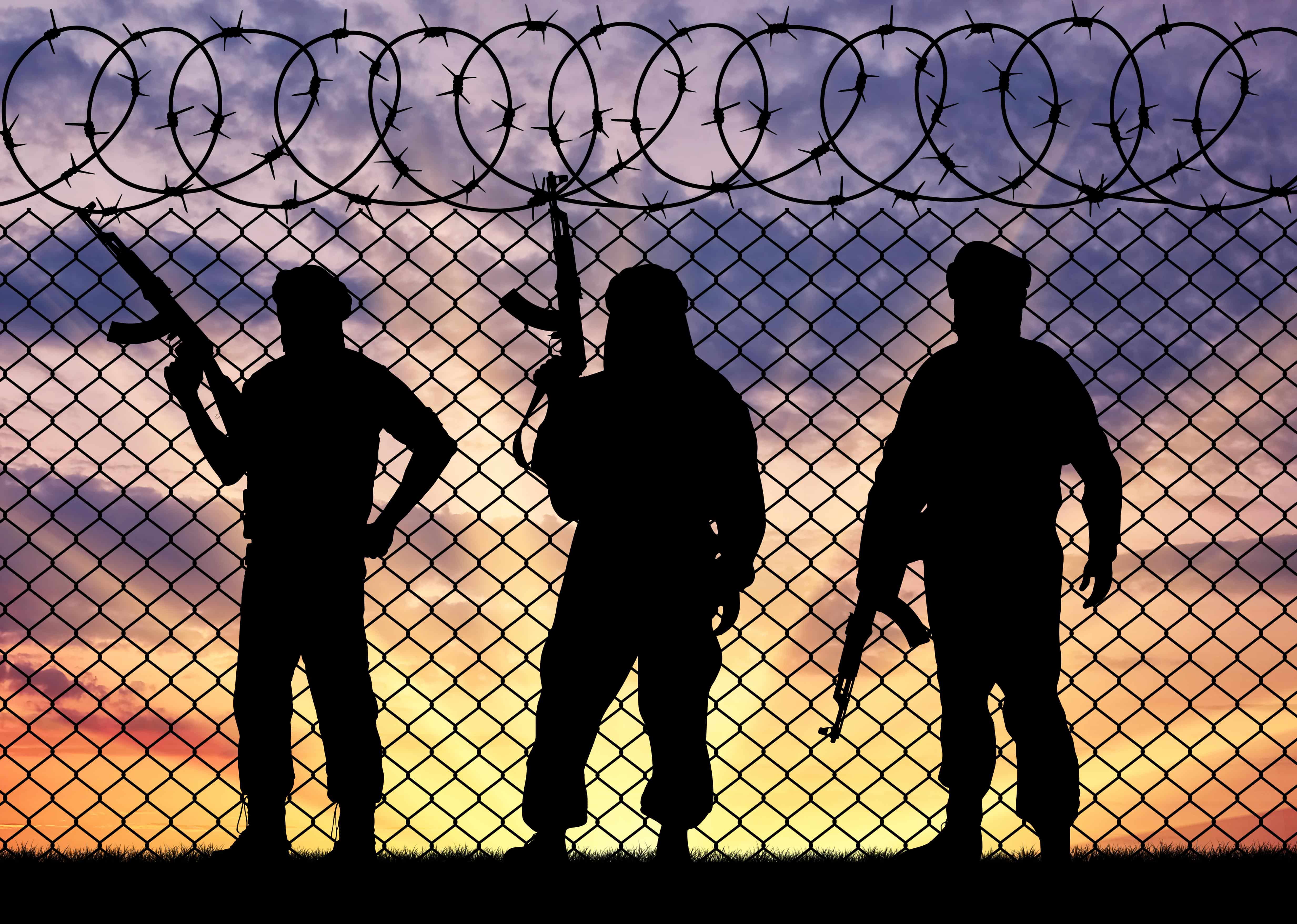 Concept of terrorism. Silhouette terrorists near the border fence in the background at sunset