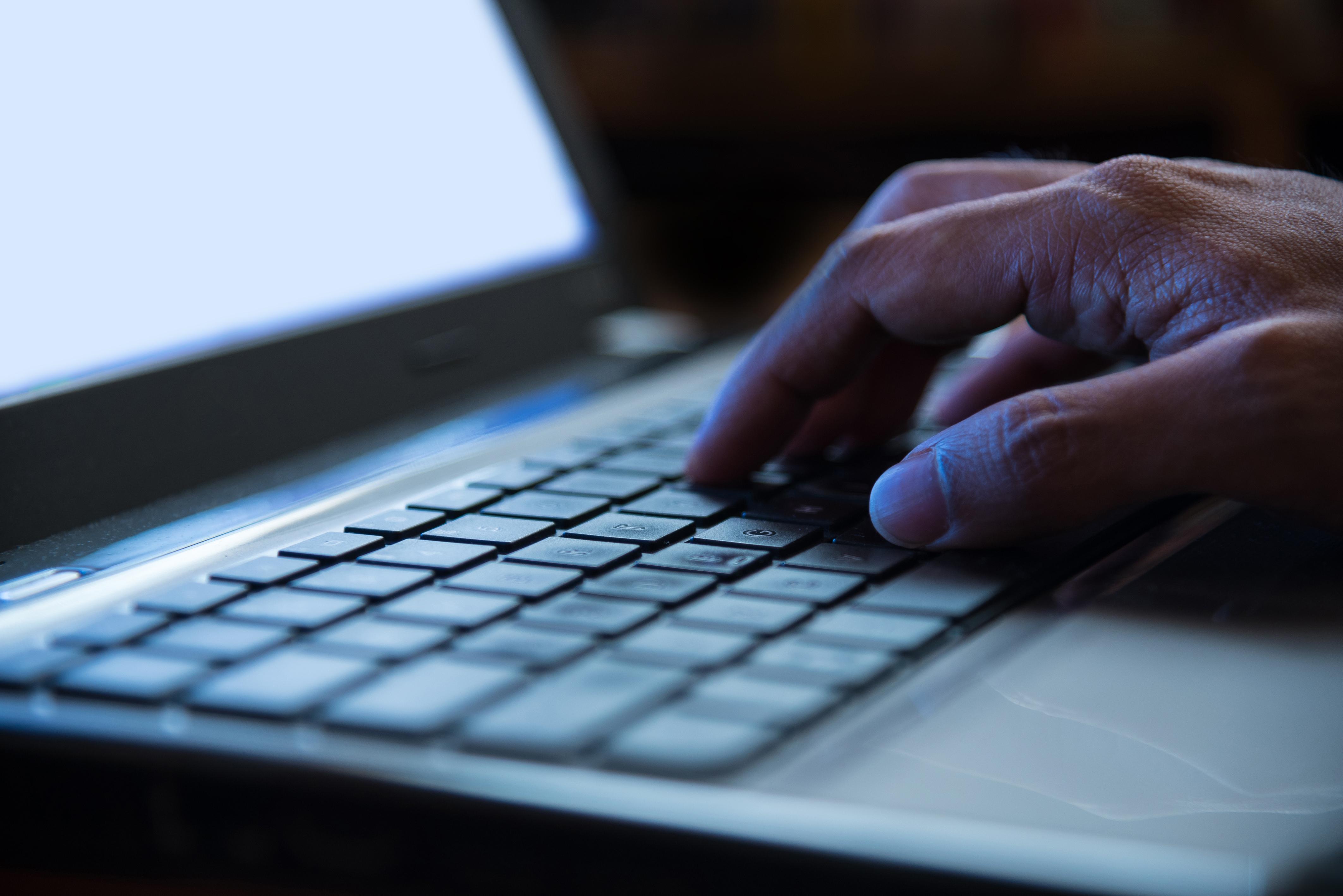 Selective focus on man hand typing laptop/PC/computer keyboard in night dark tone low key