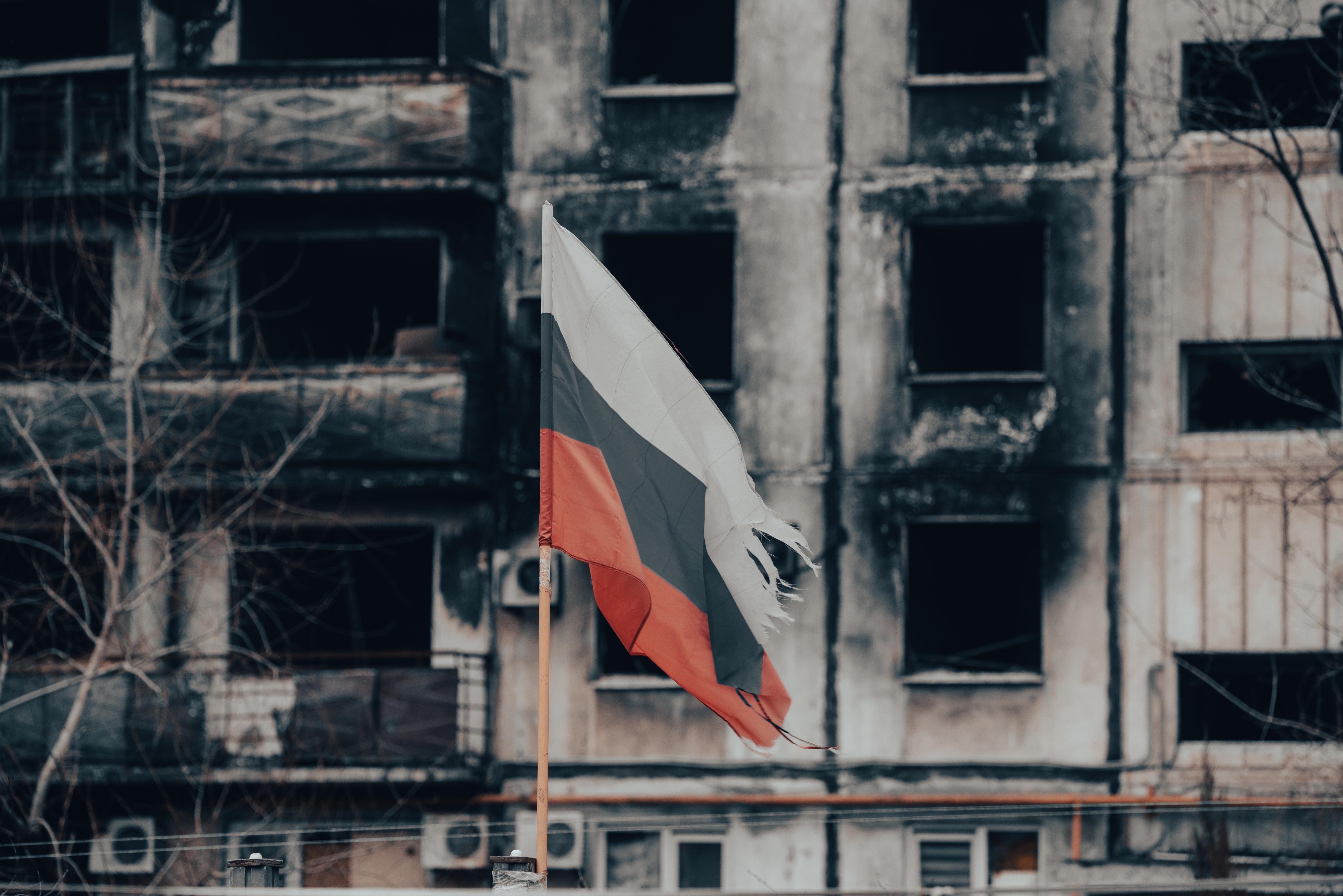 tricolor flag of Russia against the background of destroyed and burnt houses war in Ukraine